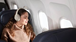 Woman sitting on an airplane wearing Sony WH-1000XM4 headphones in beige colorway