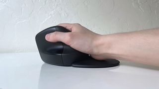 The HP 925 ergonomic vertical mouse in a user's hand on a white desk